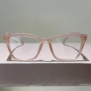 Detail der rosa Cat-Eye-Brillenfassung mit Goldakzenten auf grauem Grund