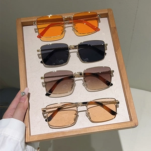 Detail of square gold metal sunglasses with orange, black, and gradient lenses on a tray