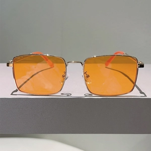 Detail of square gold metal frame sunglasses with vibrant orange translucent lenses