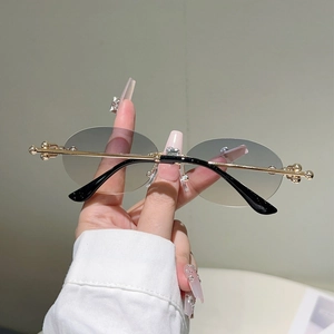 Détail de lunettes de soleil ovales sans monture avec rotule dorée et pont en métal gravé