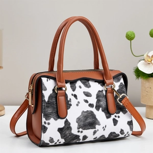 Vintage cow print tote bag with brown handles and shoulder strap on white desk