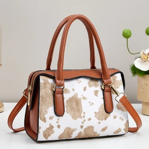 Close-up of cow print Boston bag with brown faux leather straps and golden hardware