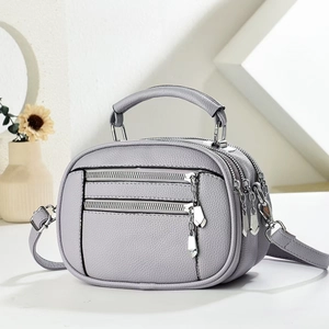 Close-up of a light grey multi-layer crossbody bag with lychee grain and silver zippers