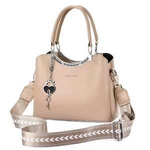Beige faux leather handbag with wide shoulder strap and heart charm on white background