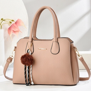 Détail du sac à main rose grainé avec pompon marron et finitions métalliques élégantes