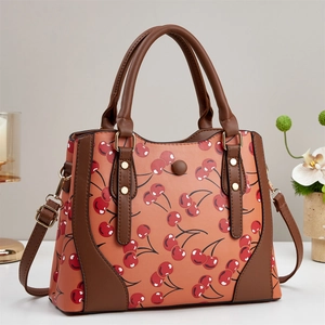 Detail of orange-brown crossbody bag with red cherry prints and golden metal studs
