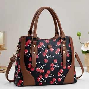 Crossbody bag with cherry print and brown leather straps on a minimalist background