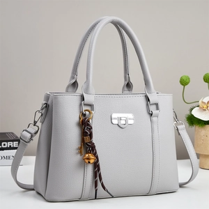 Close-up of light grey lychee leather handbag with silver lock and decorative charm