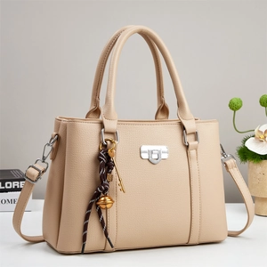 Detail of beige lychee grain leather bag featuring silver lock and decorative woven pendant