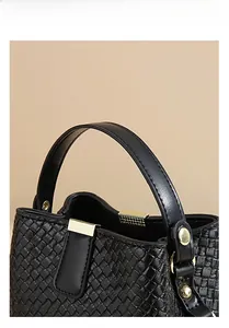 Close-up of black woven leather bucket bag with gold metal buckle and round handle