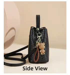 Side view of black woven bucket bag with brown bear pendant and adjustable shoulder strap