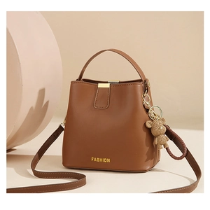 Detail of a brown bucket bag with a fashion logo and a woven bear pendant accessory