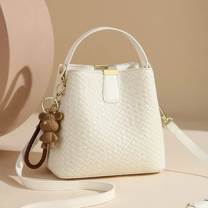 Sac seau blanc tressé avec détails dorés et pendentif ours sur fond minimaliste