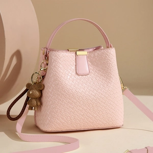 Pink woven bucket bag with bear pendant and gold hardware on warm minimal background