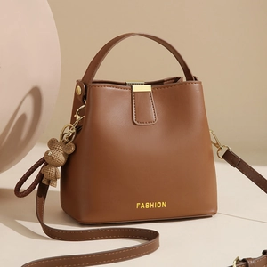 Brown leather bucket bag with top handle, adjustable strap, and bear charm