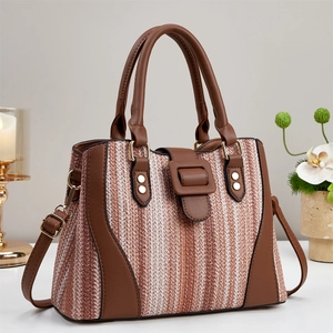 Fashionable brown woven tote bag with leather trim and gold buckle shown on a white table