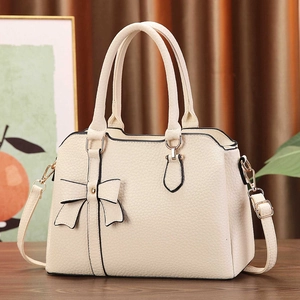 Close-up of litchi texture beige bag with bow detail and gold-tone hardware