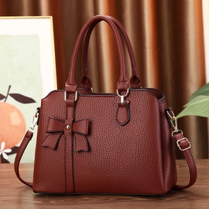 Close-up of deep red lychee texture leather handbag with bow and metal rivet detail