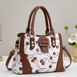 Détail du sac en cuir blanc avec imprimé cerise, boucle brune et accents en métal doré