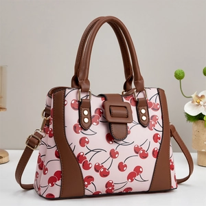 Détail du sac bandoulière rose à motif cerise avec finitions cuir brun et métal doré