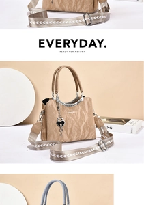 Close-up of khaki pleated handbag featuring heart pendant and patterned strap detail