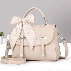 Detail of beige faux leather handbag featuring silver hardware and a pink silk scarf bow