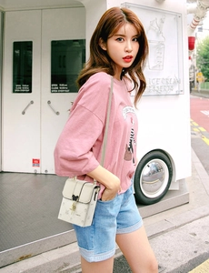 Close-up of beige mini crossbody bag with logo print and gold tassel hardware detail