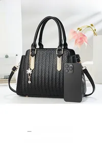 Close-up of black woven shoulder bag with gold hardware and phone for scale reference