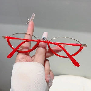 Detail of red and gold cat-eye glasses frame held by hand against a neutral background