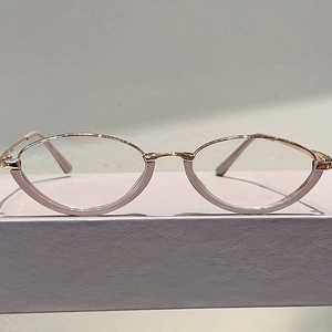 Detail view of pink and rose gold cat-eye glasses frame on a gray display case
