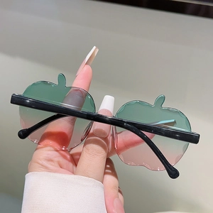 Dettaglio di occhiali da sole a forma di mela con lenti sfumate verde-rosa e aste nere