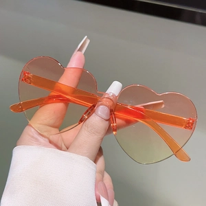 Close-up of heart-shaped rimless sunglasses with orange gradient lenses and clear temples