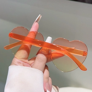 Detail of heart-shaped rimless sunglasses featuring orange gradient lenses and clear frames