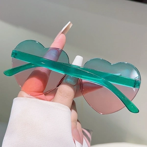 Detail of heart-shaped sunglasses with green to pink gradient lenses and clear temples