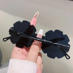 Detail view of black flower-shaped rimless sunglasses held by hand for kids' parties