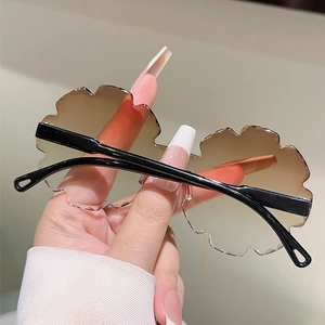 Detail of flower shaped rimless sunglasses with gradient brown lenses and black temples