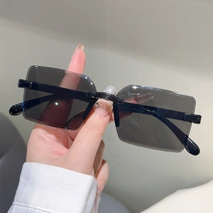 Close-up of hand holding grey rimless rectangular sunglasses with metal bridge