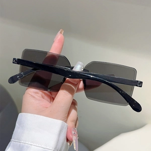 Close-up of frameless square sunglasses with black tinted lenses and polished temples