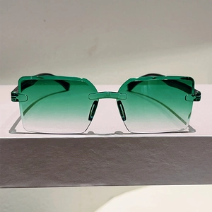 Detail of rimless square sunglasses with green gradient lenses on a beige pedestal