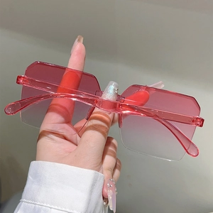Close-up of red gradient frameless rectangular sunglasses held against a neutral wall