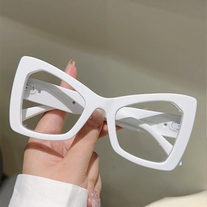 Close-up of glossy white oversized cat-eye glasses held by hand on a neutral backdrop