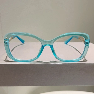 Detail of teal cat-eye glasses frame with golden metal hinges on a display stand