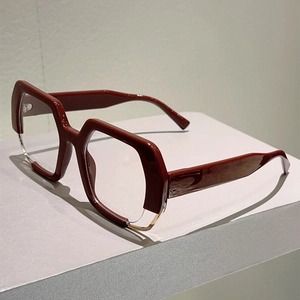 Detail of burgundy geometric eyewear frame with gold metal accents on a grey stand