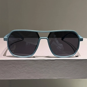 Close-up of matte grey-blue pilot sunglasses with double-bridge frame on textured stand
