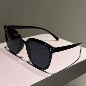 Close-up of black cat-eye sunglasses with triple dot rivets on a grey display block