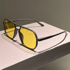 Classic aviator sunglasses with matte black frames and vibrant yellow lenses on a grey pedestal