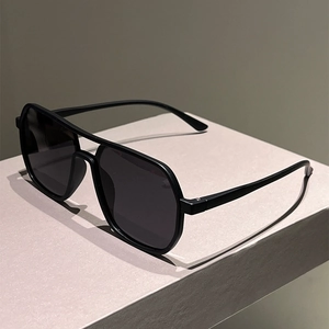 Detail view of black double-bridge aviator sunglasses on a minimalist grey box stand