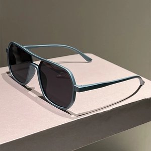 Detail of matte blue-grey double-bridge aviator sunglasses on a minimalist display stand