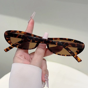 Detail view of oval tortoise shell sunglasses with brown lenses held by hand