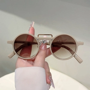 Détail de lunettes de soleil rondes rétro beiges avec barre dorée et verres dégradés bruns